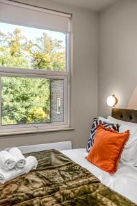a bedroom with a bed with an orange pillow and a window at Consort 3A- 4 | Stylish Compact Studio with Kitchennette and Full Communal Kitchen in London +5 photos