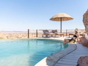 two women sitting next to a swimming pool with an umbrella at Onduli Ridge in Twyfelfontein