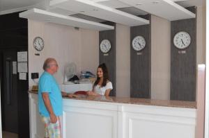 a man and a woman standing at a counter with clocks at Kalif Hotel in Ayvalık