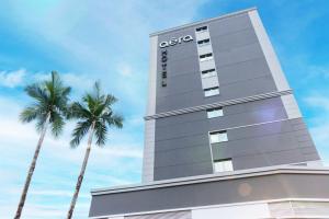 a tall building with two palm trees in front of it at Aera São José Floripa - Hotel com café da manhã a 10 min do CentroSul in São José