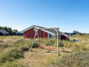 a swing set in a field with a red barn at Holiday Home Bertie - 700m from the sea by Interhome in Hirtshals