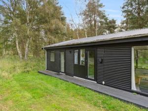 a black cabin with a wooden porch in a field at Holiday Home Shayene - 2-5km from the sea by Interhome in Læsø