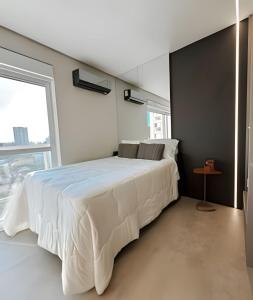 a bedroom with a large white bed with a window at Estúdio Praga: Vista para o por do sol in Criciúma