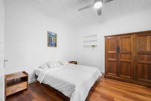 a white bedroom with a bed and a wooden cabinet at Domaine Honore - Case Créole dans Jardin Tropical in Sainte-Rose +22 photos