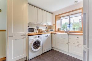 a kitchen with white cabinets and a washer and dryer at Rowan Tree - Breakish in Broadford