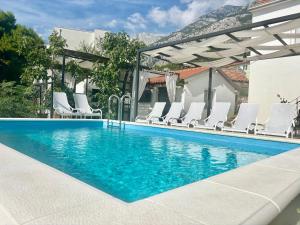 a swimming pool with white chairs and an umbrella at Summer Apartment in Makarska