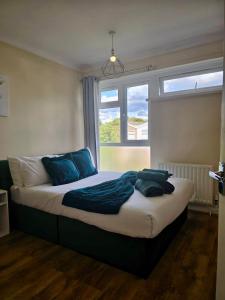 a bed with blue pillows in a room with a window at Gorgeous 3 bed House - Free Parking near Elizabeth line in Abbey Wood