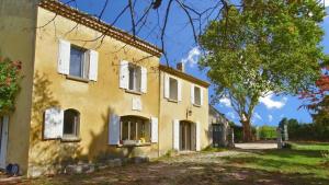 a yellow house with white windows and a tree at Le Gite au coin du feu in Cabannes