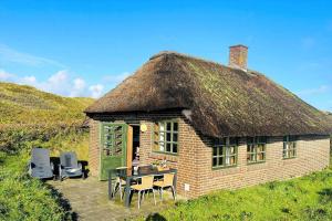 a hut with a grass roof with a table and chairs at 21300-Ulfborg-Somaerkevej-6-b in Vedersø Klit