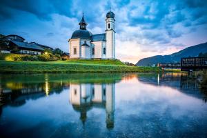 a church with a clock tower sitting on top of a body of water at Seefeld ALPIN Apartments in Seefeld in Tirol