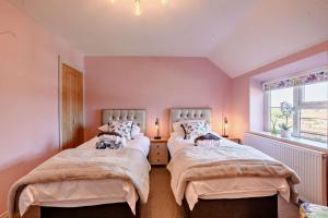 deux lits dans une chambre aux murs roses et une fenêtre dans l'établissement Victoria Cottage - Wensum Retreats, à Gunthorpe 18 autres photos