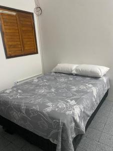 a bed with a gray and white comforter and a window at RS Pousada in Bayeux