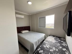 - une petite chambre avec 2 lits et une télévision dans l'établissement Apartamento Vista Mar Mirim 2 Dormitorios suite com Wifi para até 8 pessoas 1 vaga de estacionamento, à Praia Grande
