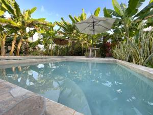 a large swimming pool with an umbrella and trees at Zanzllywood Uroa Beach Suites Hotel Apartment in Dikoni