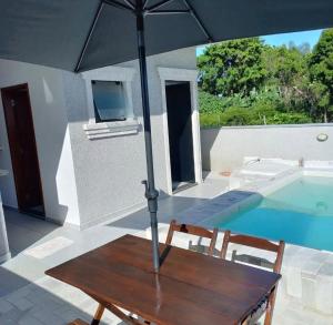 a table with an umbrella next to a swimming pool at Casa com piscina! Descanso e Lazer in Itapoa