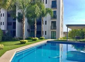 a swimming pool in front of a building with palm trees at La PRIMAVERA APARTMENT IN CUERNAVACA in Cuernavaca