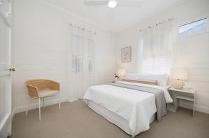 une chambre blanche avec un lit et une chaise dans l'établissement Historic CBD Miner's Cottage, à Brisbane