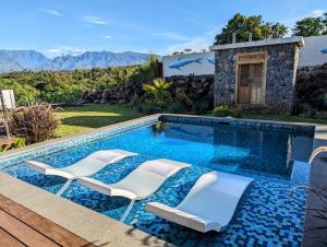une piscine avec des chaises blanches et une maison dans l'établissement La villa Blue Banian, à Saint-Pierre