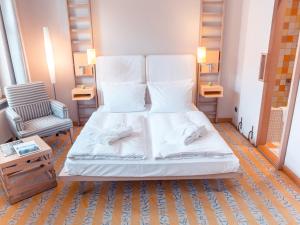 ベルリンにあるホテル ブライブトロイ ベルリン バイ ゴールデン チューリップのベッド(白いシーツ付)と椅子が備わります。