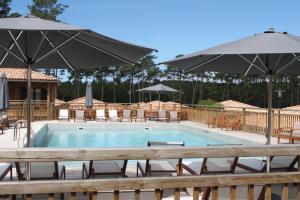 a swimming pool with tables and chairs and umbrellas at Domaine du Ferret Restaurant & Spa in Cap-Ferret