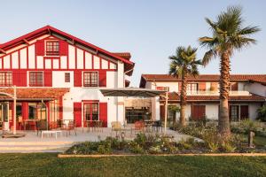 a red and white house with a patio and palm trees at Hôtel INDARRA & SPA - Piscine in Arbonne