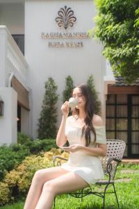 a woman in a white dress sitting on a chair drinking from a glass at Rachamankha Flora House in Chiang Mai