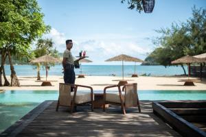 Ein Mann steht mit einem Tisch und Stühlen auf einem Steg am Strand. in der Unterkunft Kuara Lombok in Bumbang