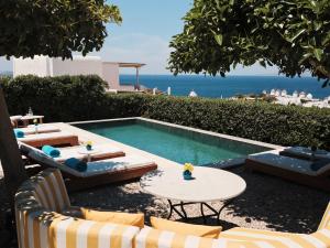 a swimming pool with chairs and tables and the ocean at Belvedere Mykonos - Hilltop Rooms & Suites - The Leading Hotels of the World in Mikonos
