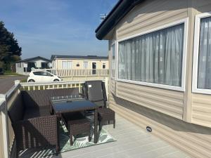 eine Terrasse mit Tisch und Stühlen auf einem Deck in der Unterkunft The Retreat 36 - Golden Palm Resort - Meadow Lakes Caravan Hire in Chapel Saint Leonards