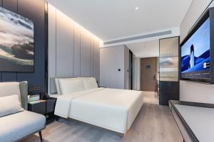 Atour Hotel Shanghai North Bund Dalian Road في شانغهاي: غرفة نوم بسرير ابيض وتلفزيون