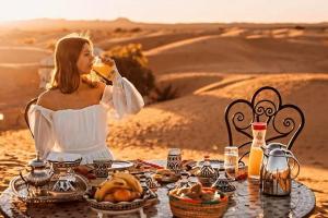 Eine Frau sitzt an einem Tisch in der Wüste und isst Essen. in der Unterkunft luxury desert night camp in Merzouga