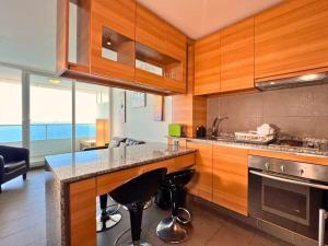 a kitchen with wooden cabinets and a counter with bar stools at Hermoso departamento en Costa Horizonte in Concón
