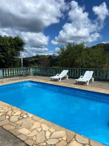a blue swimming pool with two white chairs next to it at Espaço dos Lobato in Miguel Pereira