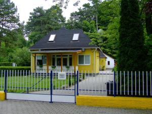 a yellow house with a black roof behind a fence at Relax Apartmans in Balatonszemes
