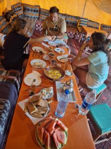 メルズーガにあるDesert Camel Trekの食べ物を囲んでテーブルの周りに座っている人々のグループ +32枚の写真