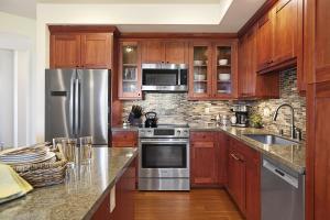 a kitchen with wooden cabinets and a stainless steel refrigerator at Poipu Retreat with Golf Ocean Views and AC in Koloa