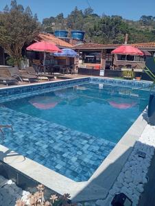 a pool with blue water and red umbrellas at Pousada Beija flor in Extrema