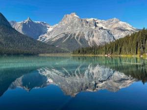 a reflection of a mountain in a lake with trees at Chancellor Peak 1BR and Loft Wooden Cabin near Lake Louise in Beaverfoot