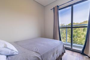 a bedroom with a bed and a large window at ApTropea: Conforto, Natureza e o Som do Mar in Praia Guaratuba