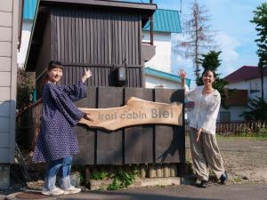 two women standing next to a sign that reads hotel cedar bid at Irori Cabin biei in Biei