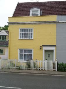 a yellow house with a white fence in front of it at Minsmere Cottage in Yoxford