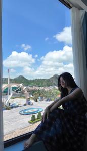 カットバ島にあるCatBa Pod Hostel & Rooftop Barのリゾートの景色を眺めながら窓枠に座っている女性