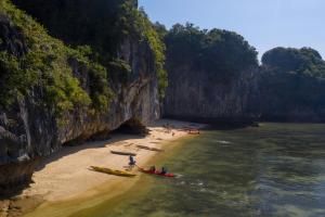 a group of people in kayaks on a beach next to a cliff at The Little Leaf Hostel - Restaurant & Rooftop Bar CatBa in Cat Ba
