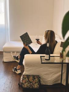 a woman sitting on a couch reading a book and a glass of wine at La Bora Roiana in Trieste +3 photos