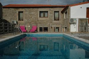 a swimming pool with two pink chairs and a building at Casa de l Telar in Duas Igrejas
