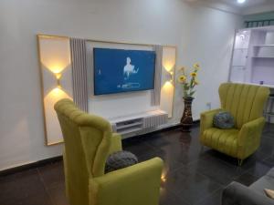 a living room with a television and two yellow chairs at Mega Pavilion Apartment Gwarinpa in Gwarinpa