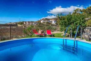 a swimming pool with two red chairs in a yard at Acogedora Casa de Madera con piscina in Güimar