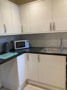 a kitchen with white cabinets and a sink and a microwave at Wookey Holiday Flat in Wookey