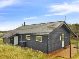 a black house with a wooden deck in a field at Holiday Home Alma - 500m from the sea by Interhome in Løkken