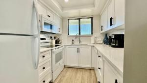 a white kitchen with white cabinets and a refrigerator at Top-floor ocean view condo with a private balcony and beachfront pool in Edgewater